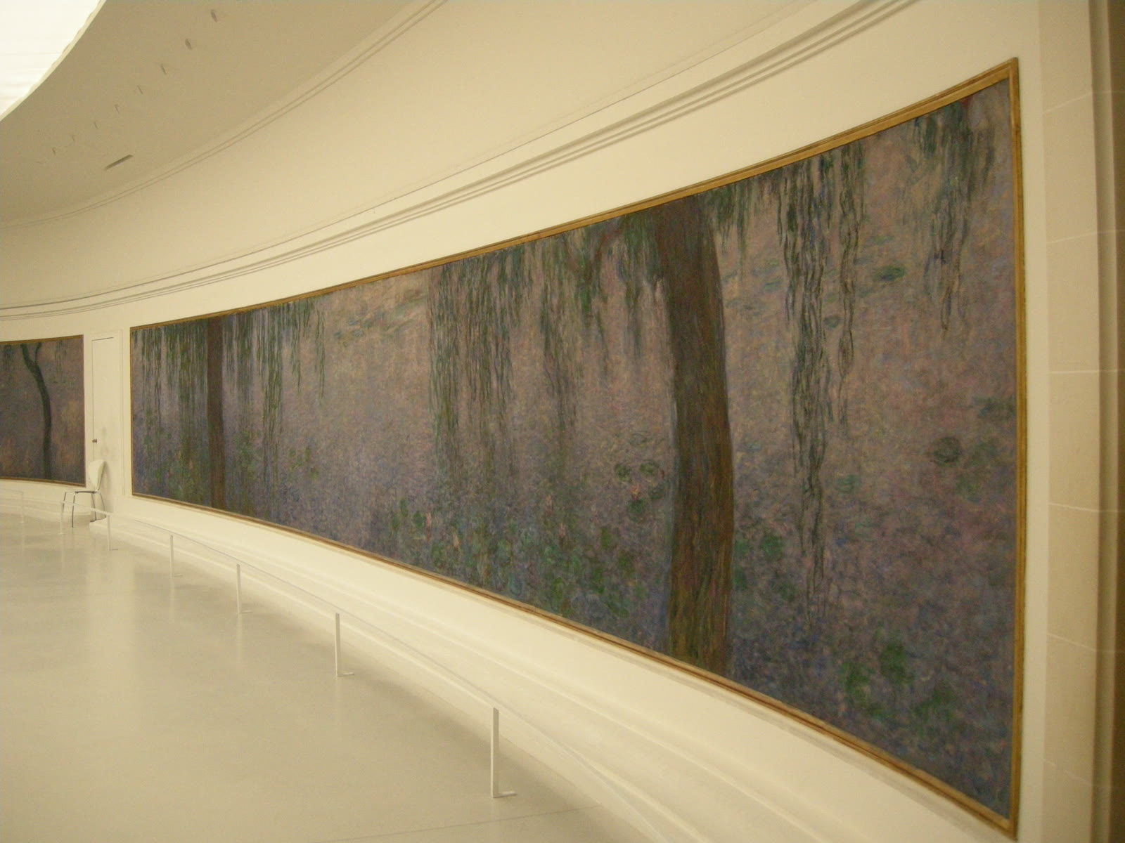 A photographed view inside the Musee de l'Orangerie, where Claude Monet's Water Lilies panels curve around an oval room.