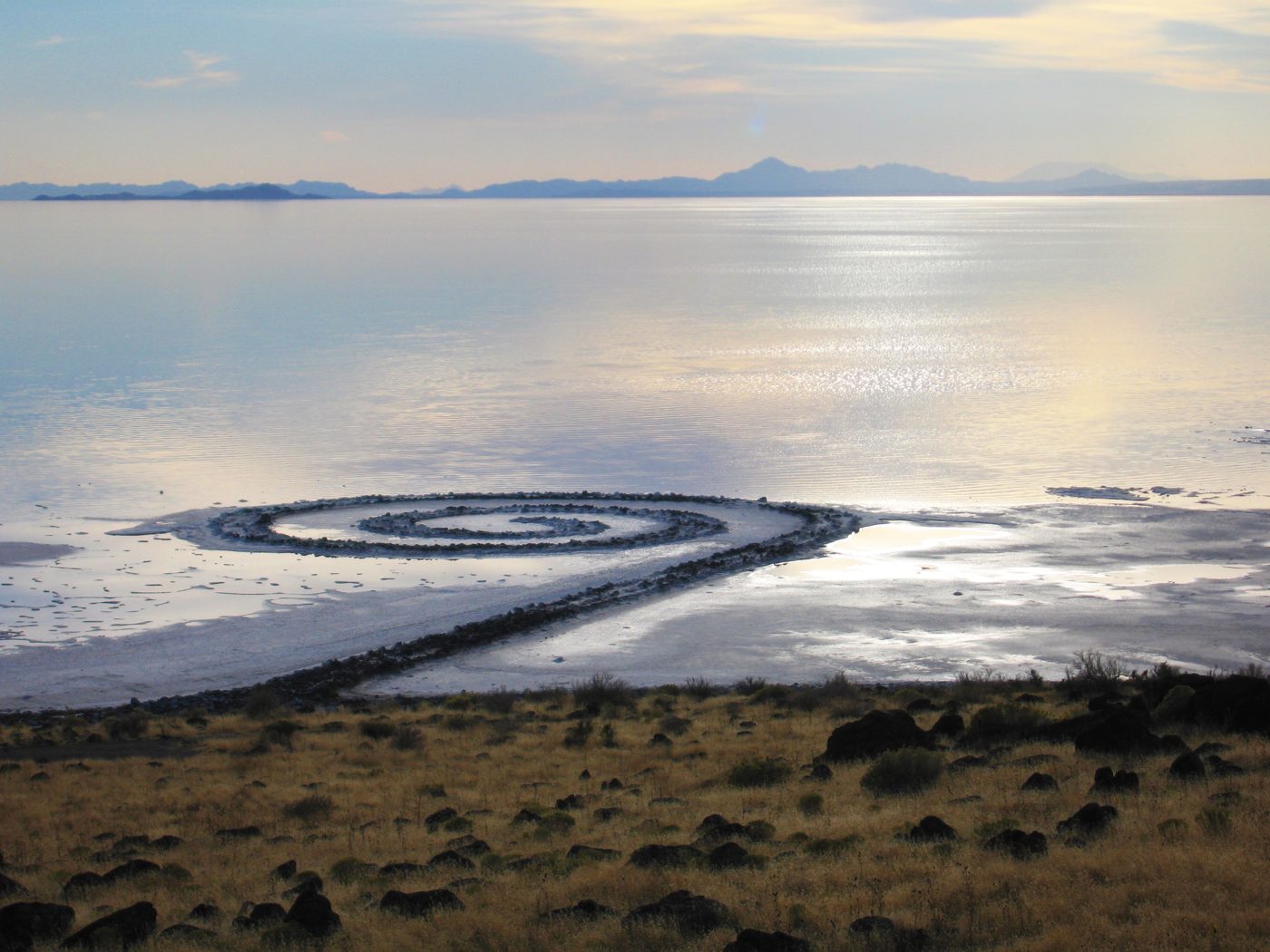 Robert Smithson's Spiral Jetty extending into the pale water of Great Salt Lake at Rozel Point, seen from an elevated hillside viewpoint.