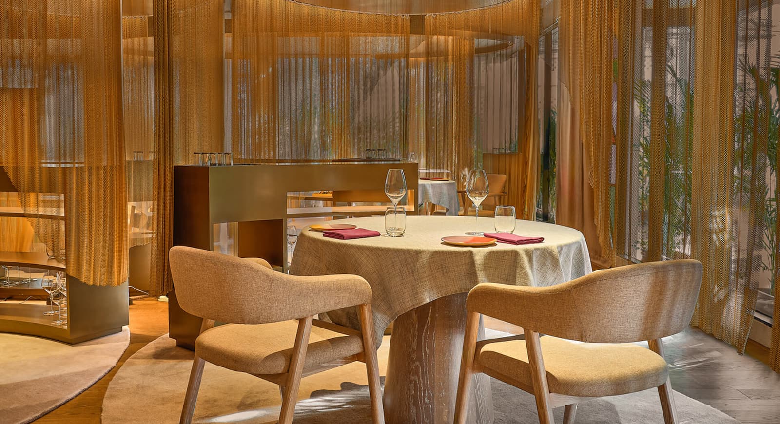 A softly lit dining table inside Gaa in Bangkok, framed by golden chain curtains and warm neutral tones.