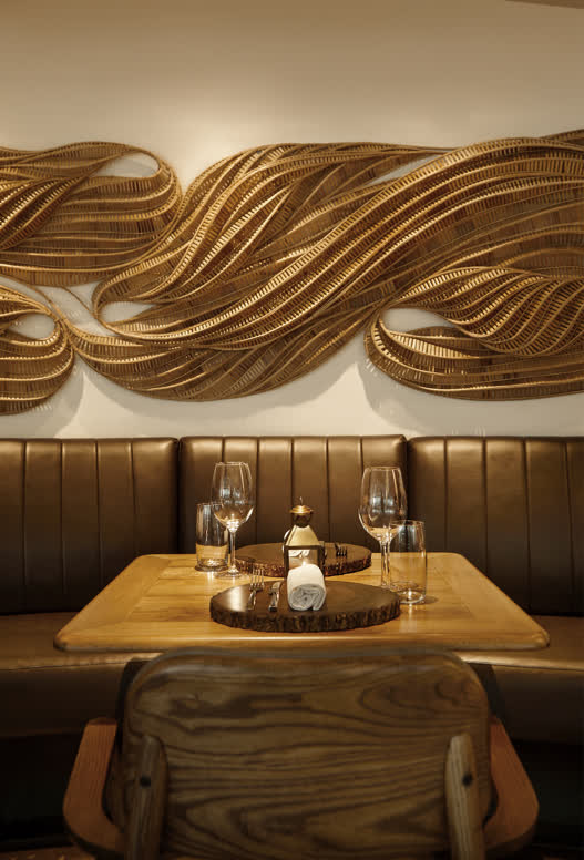 A warmly lit booth and table setting inside Le Du in Bangkok, with a woven wall installation above the banquette.