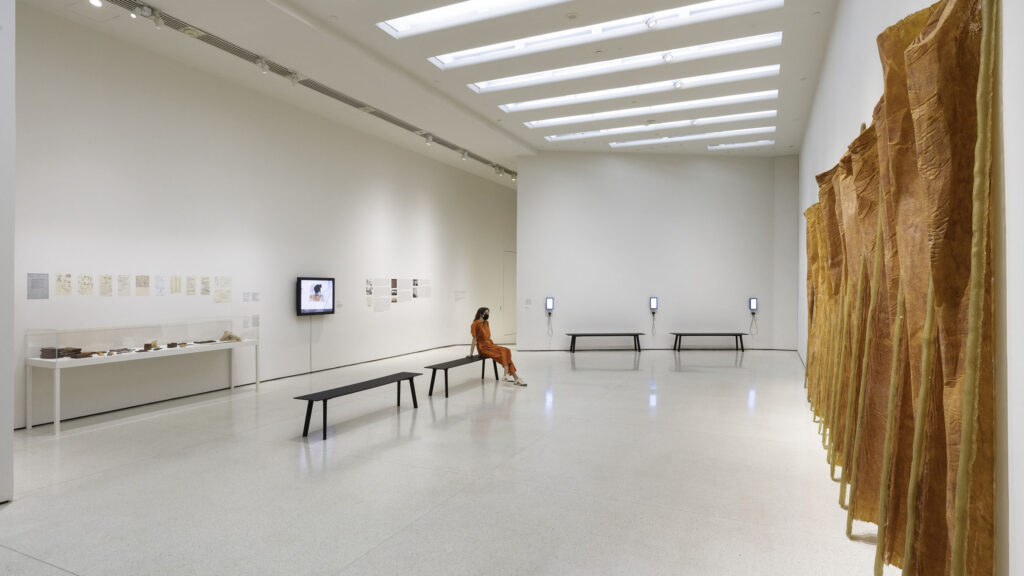 Eva Hesse's Expanded Expansion installed at the Guggenheim Museum, with repeated hanging panels and pole-like supports leaning against a white gallery wall.