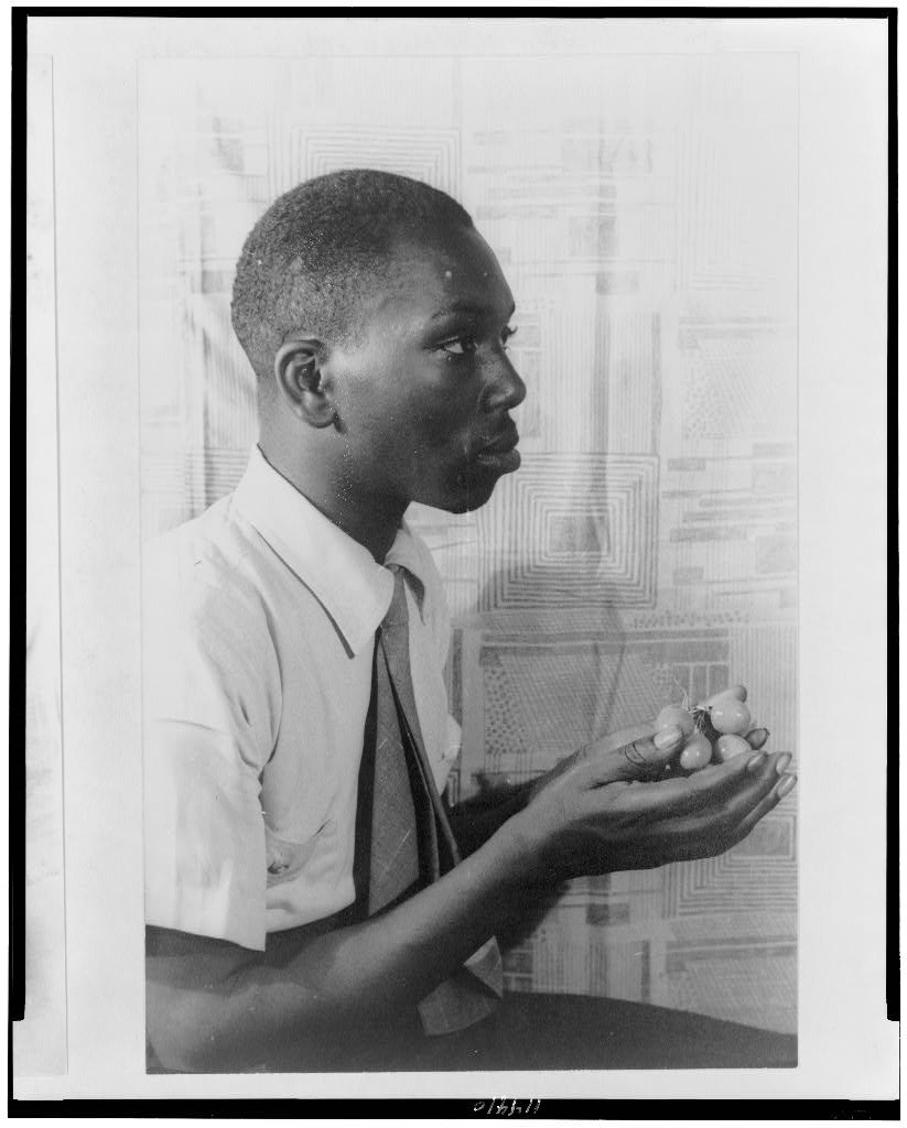A 1941 portrait photograph of Jacob Lawrence, seated and facing the camera in a dark jacket and tie.