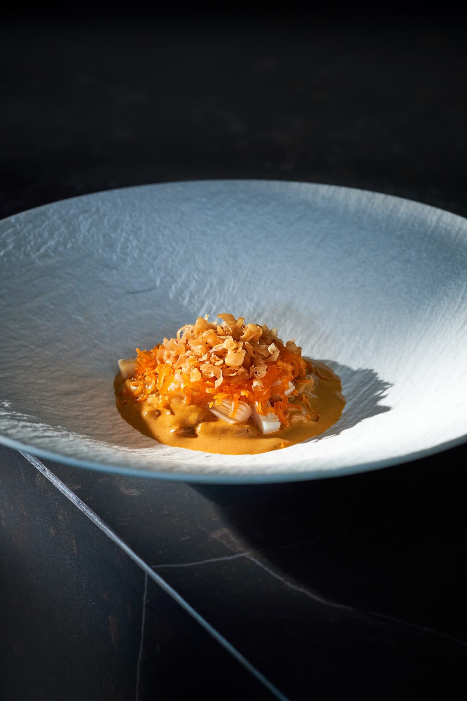 Baan Tepa's Dong Dang dish plated on a pale blue bowl with orange curry sauce and crisp garnish in direct light.