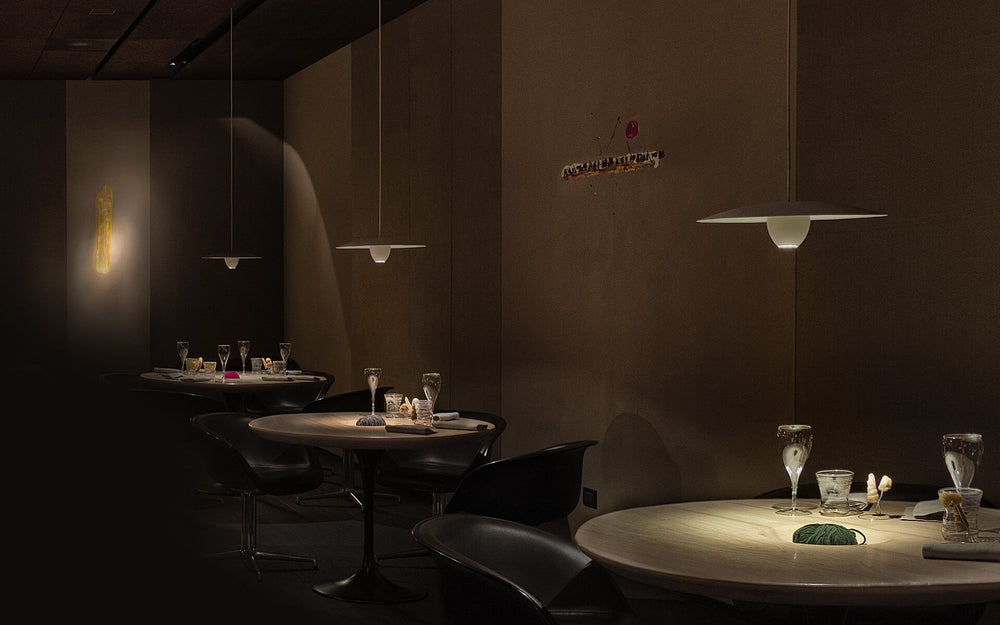Le Calandre 餐厅昏暗而安静的用餐空间，圆形木桌与黑色座椅在吊灯下被柔和照亮。