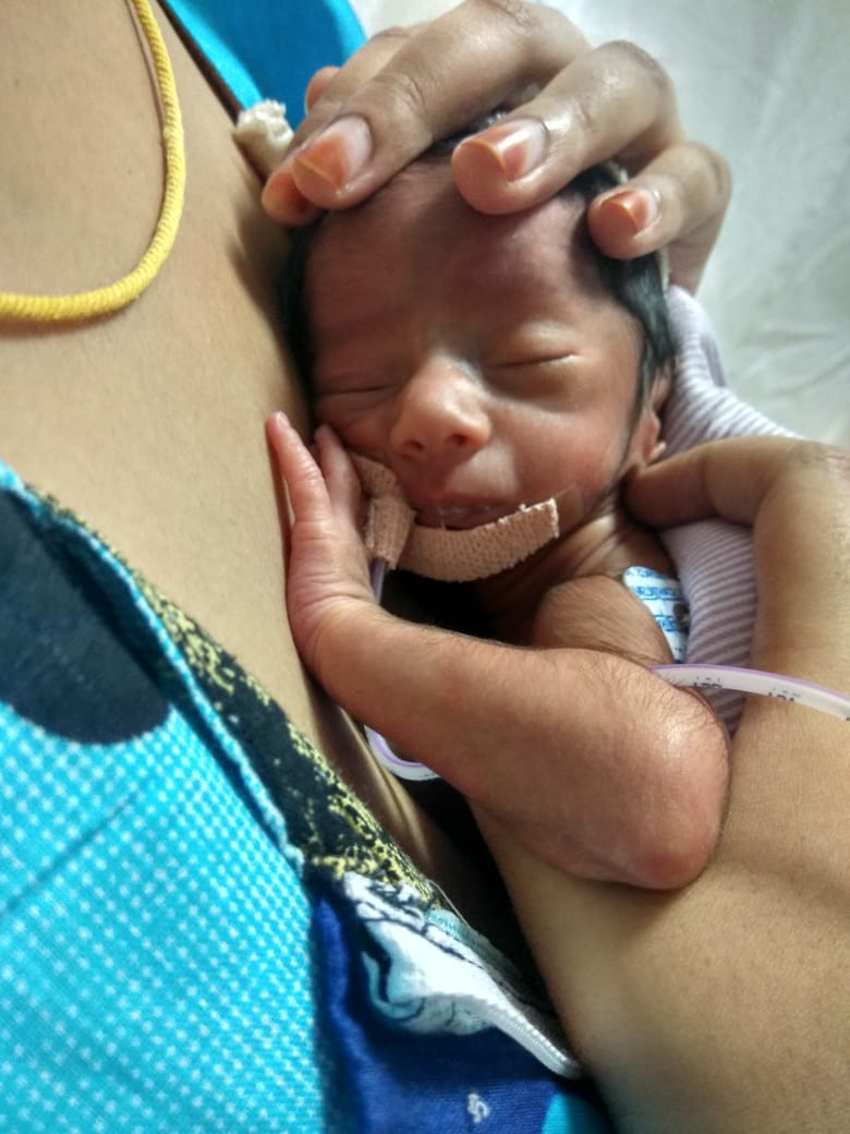 Photograph of a mother providing kangaroo mother care by holding a small newborn skin-to-skin against her chest.