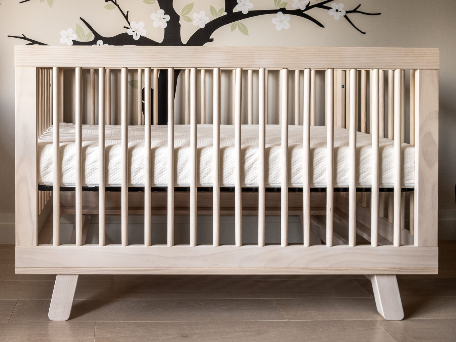 A documentary photograph of an empty wooden crib holding only a fitted mattress.