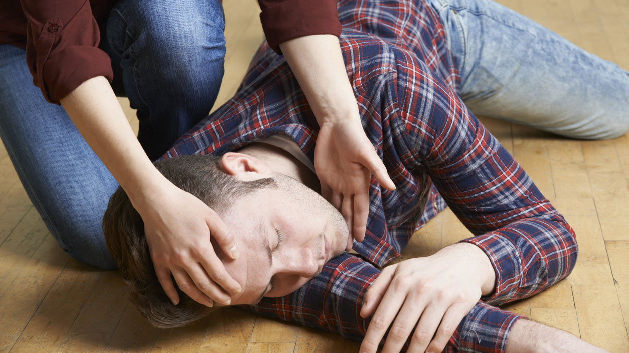 A bystander gently places a person in the recovery position during a seizure first-aid demonstration.