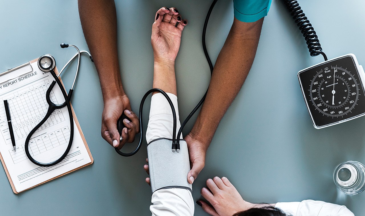 A healthcare professional places a blood pressure cuff on a seated patient's upper arm.