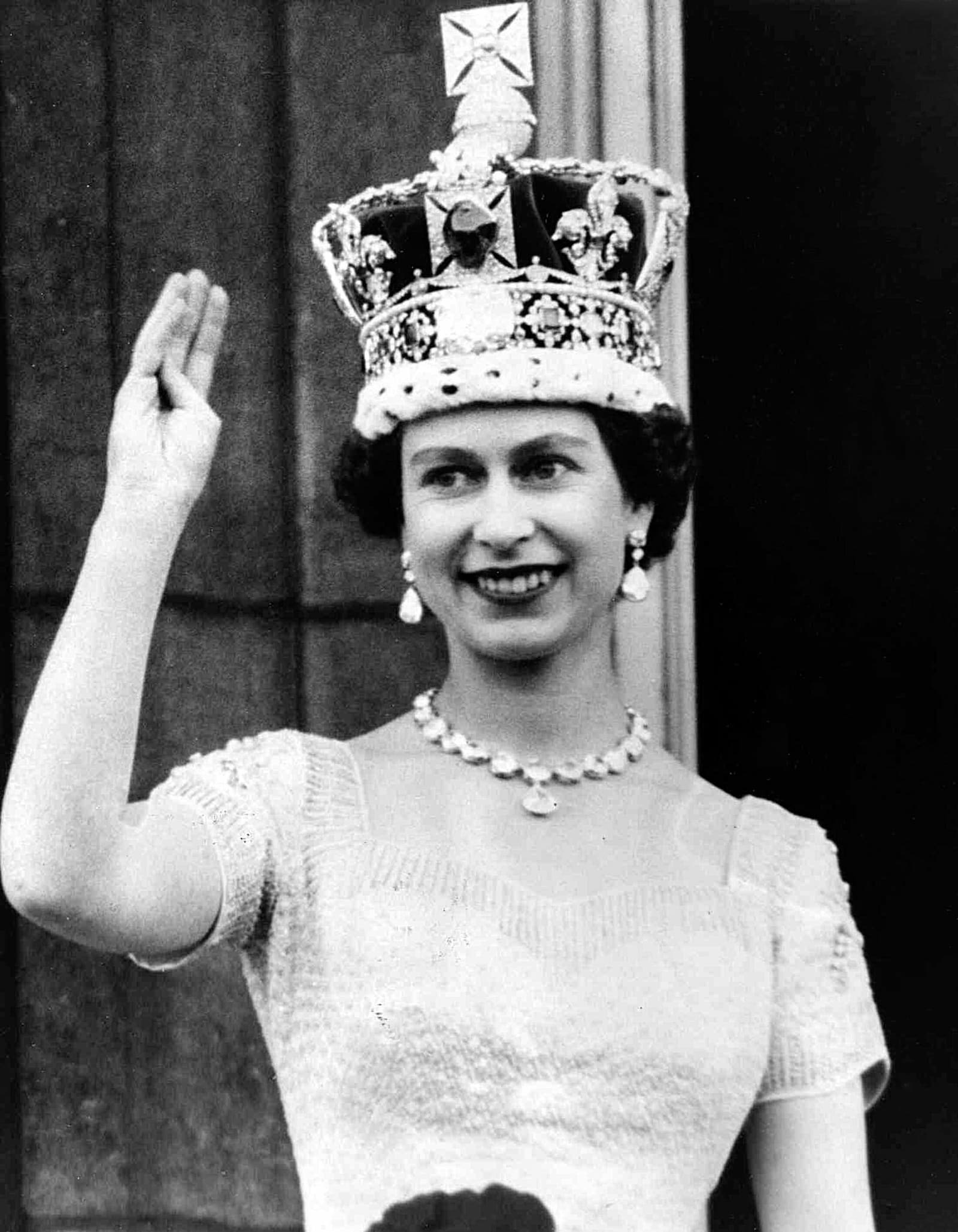 Queen Elizabeth II smiling and waving from the palace balcony after her coronation in 1953, wearing the Imperial State Crown and coronation robes.