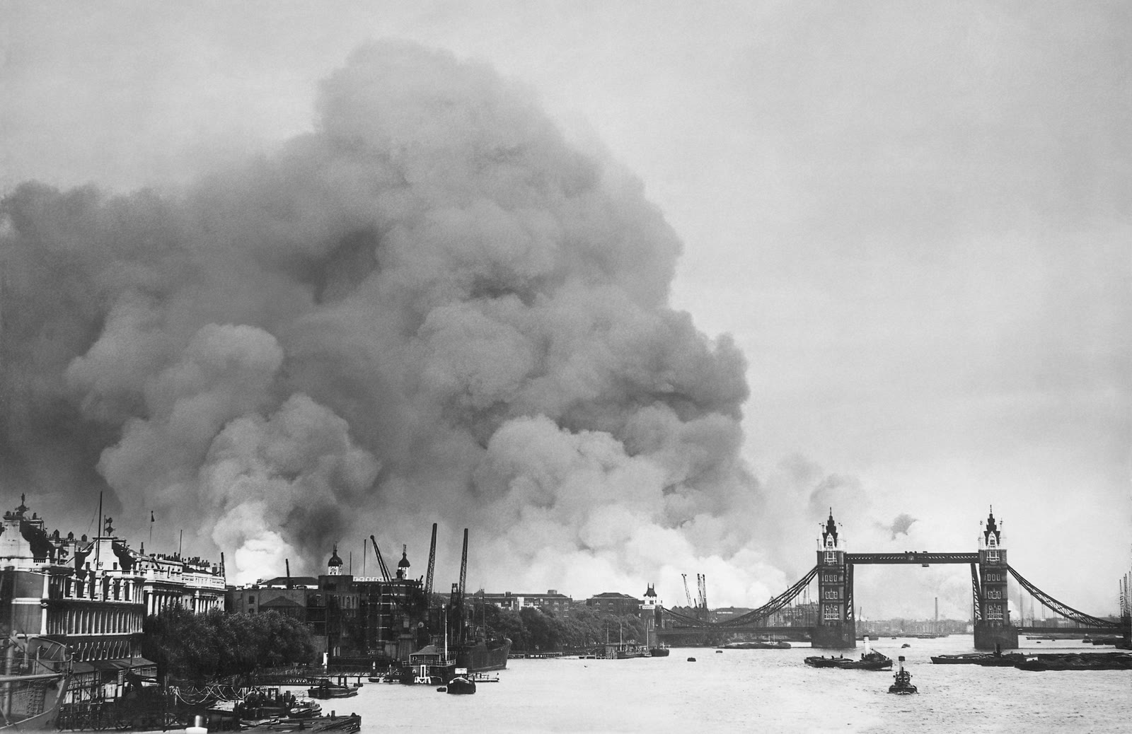Smoke rises over the River Thames and the London docks on 7 September 1940, with Tower Bridge visible in the foreground.