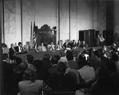A historical photograph of a Watergate Committee hearing in the Senate, with senators seated behind a long dais facing microphones and witnesses.