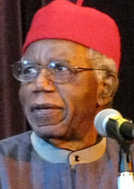 Chinua Achebe speaking at a lectern in a dark jacket and red tie in a 2008 color photograph.
