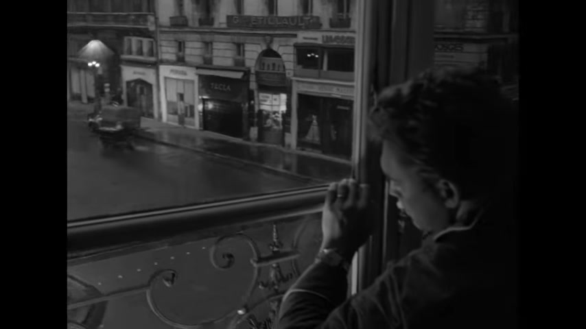 A young boy looks out from an upper-story window over a wet Paris street in a trailer still from Rififi.