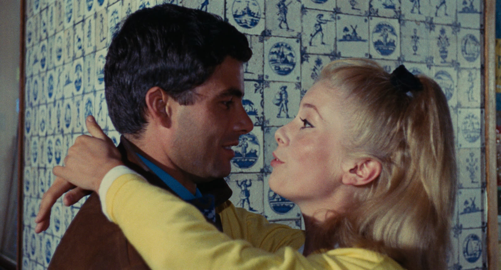 Catherine Deneuve and Nino Castelnuovo face one another in a brightly colored archival still from the 1964 film The Umbrellas of Cherbourg.
