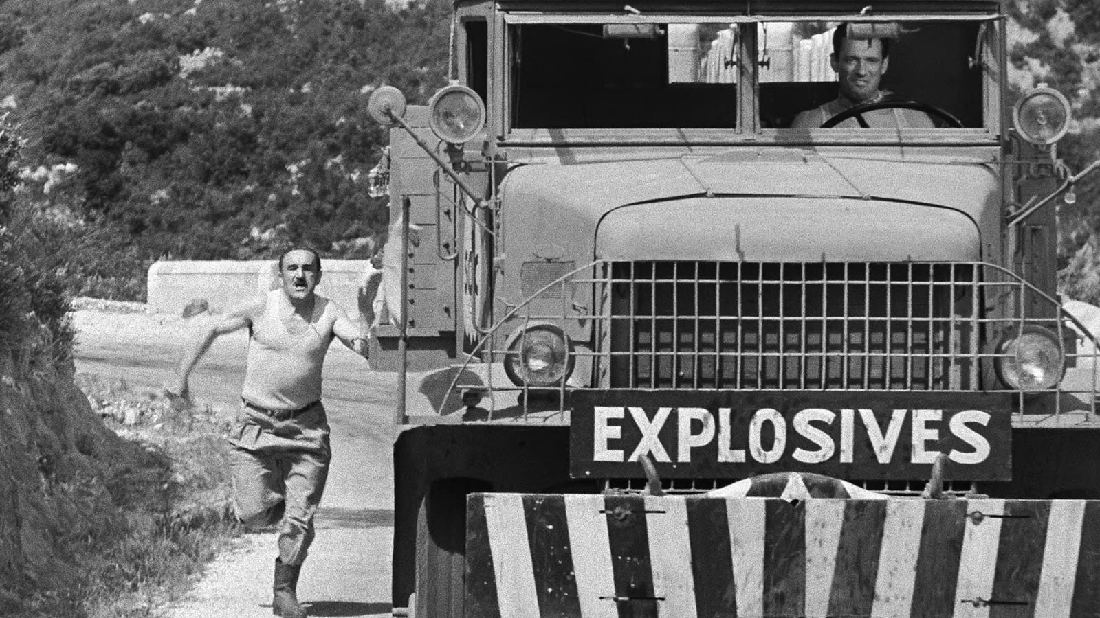 A black-and-white production still from The Wages of Fear shows an explosives truck bearing down a mountain road while a man runs beside it.