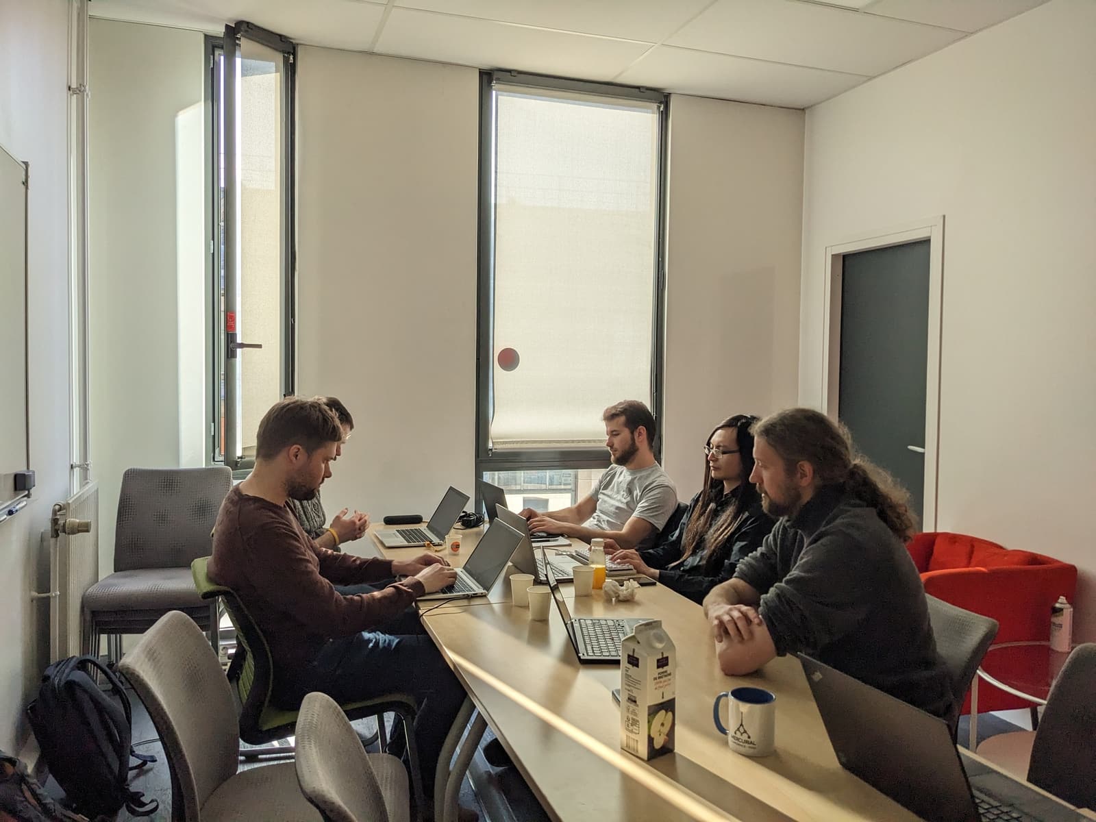 Participants in a Mercurial Paris 2023 workshop sit around a conference table with laptops while a presenter stands beside a projected screen.