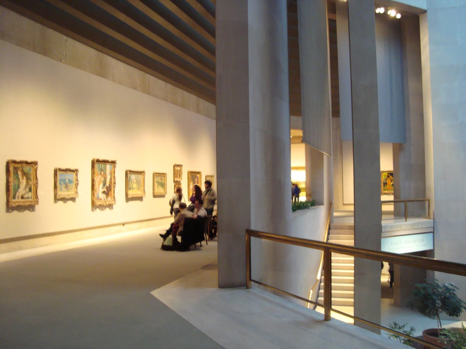 Visitors stand inside a Metropolitan Museum of Art gallery, looking across a room of framed paintings under warm museum light.