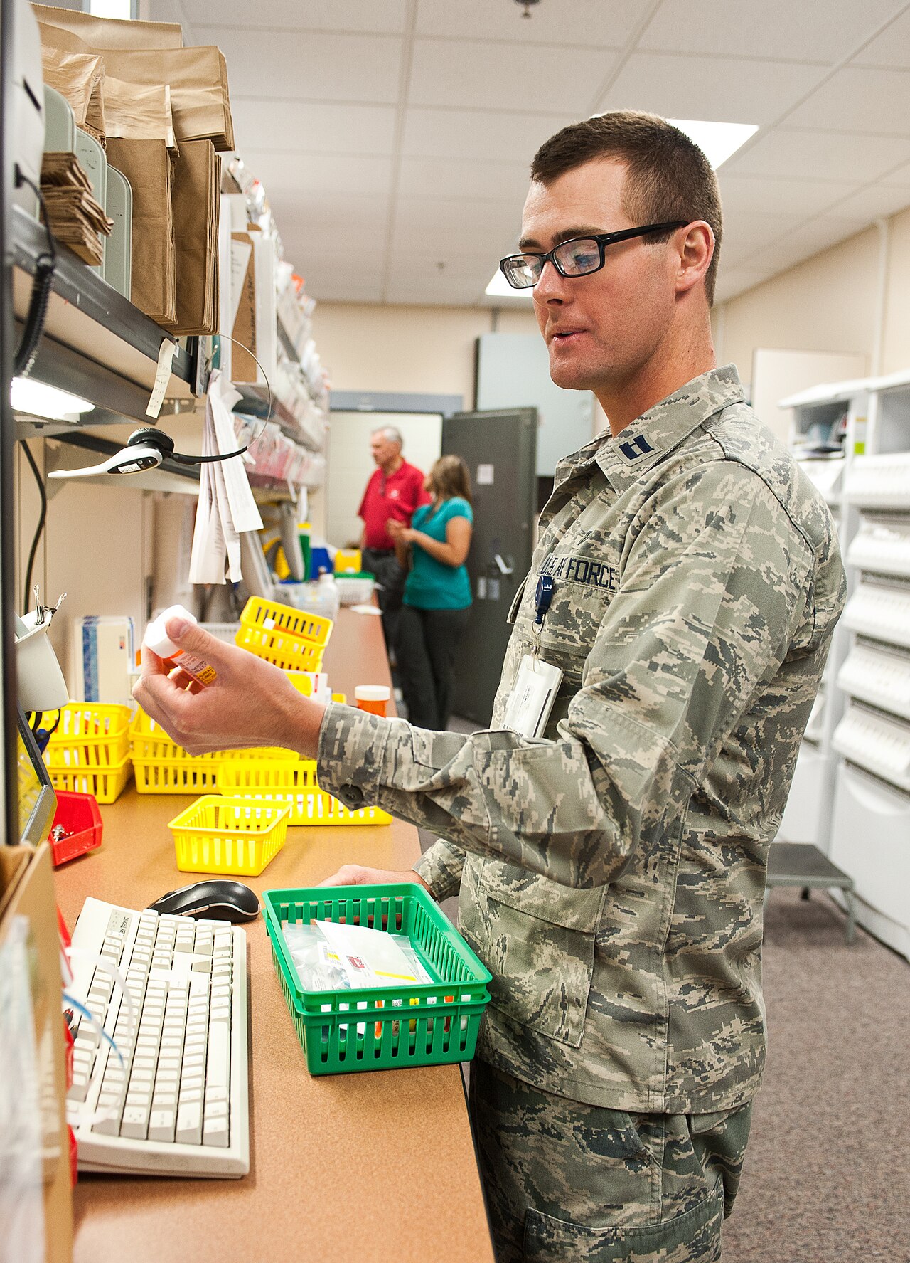 A military pharmacist in uniform verifies prescription medication at a pharmacy workstation.