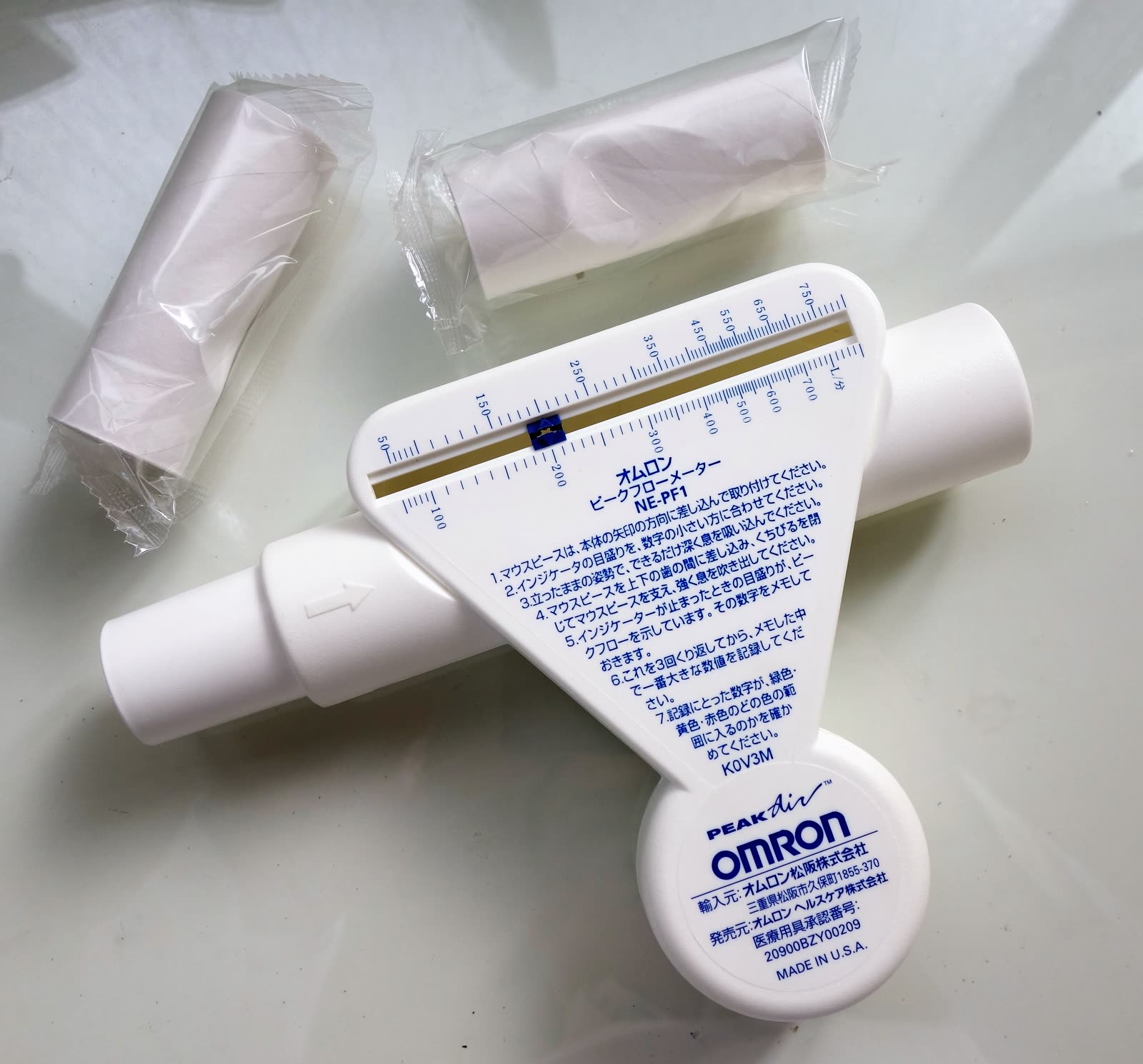 A documentary photograph shows a handheld peak flow meter with its removable mouthpiece adapter.