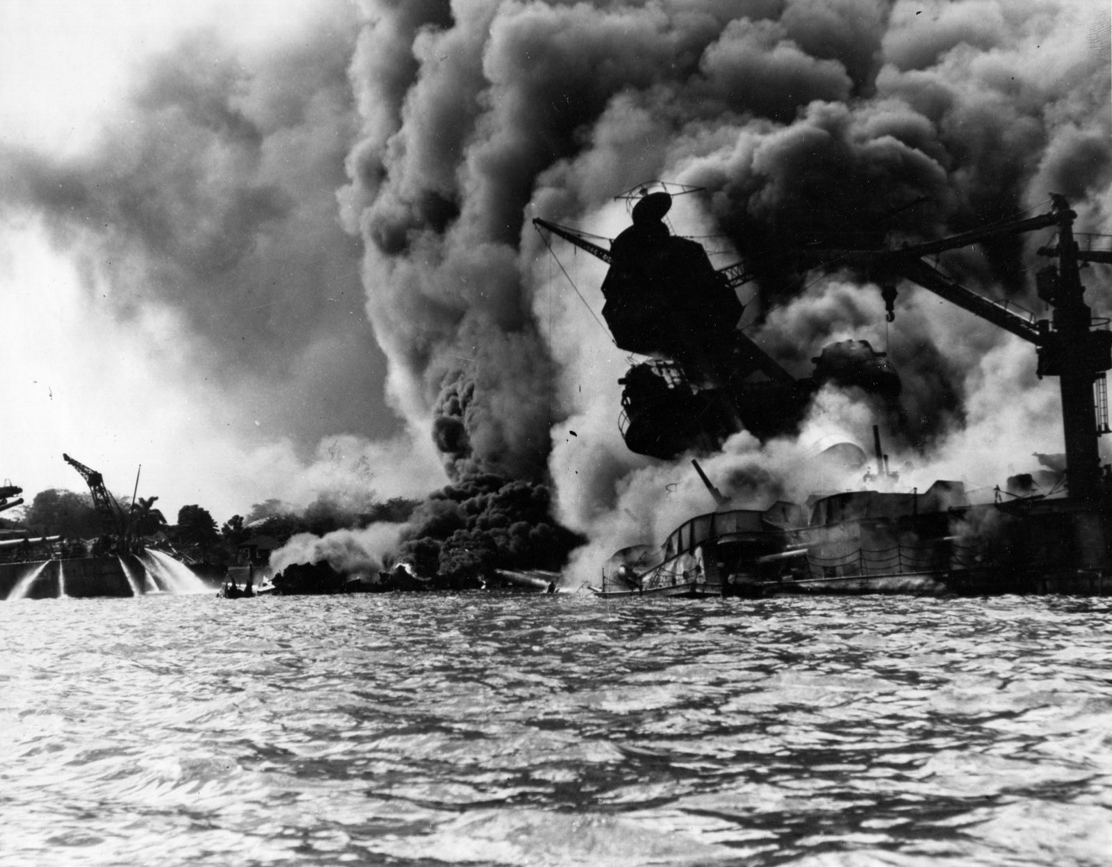 USS Arizona burning after the Japanese attack on Pearl Harbor on December 7, 1941, with sailors on USS Tennessee using hoses to push burning oil away from their ship.