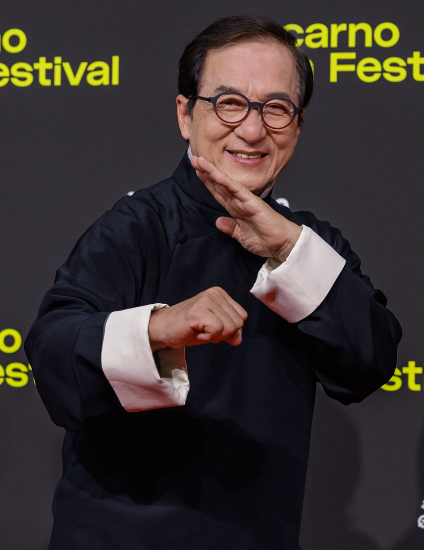 2025 年洛迦诺电影节红毯上的成龙，身穿深色西装，戴着圆框眼镜。