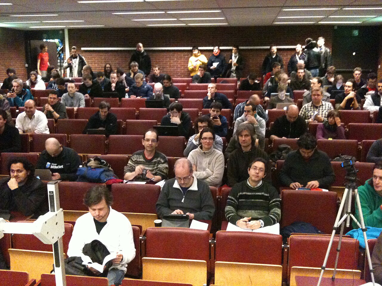 A FOSDEM developer-room audience watches a technical open-source conference talk.