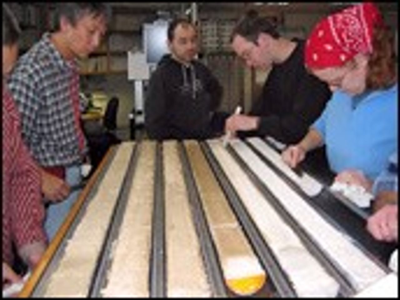 Researchers work over long ocean sediment-core sections laid out on a laboratory sample table.