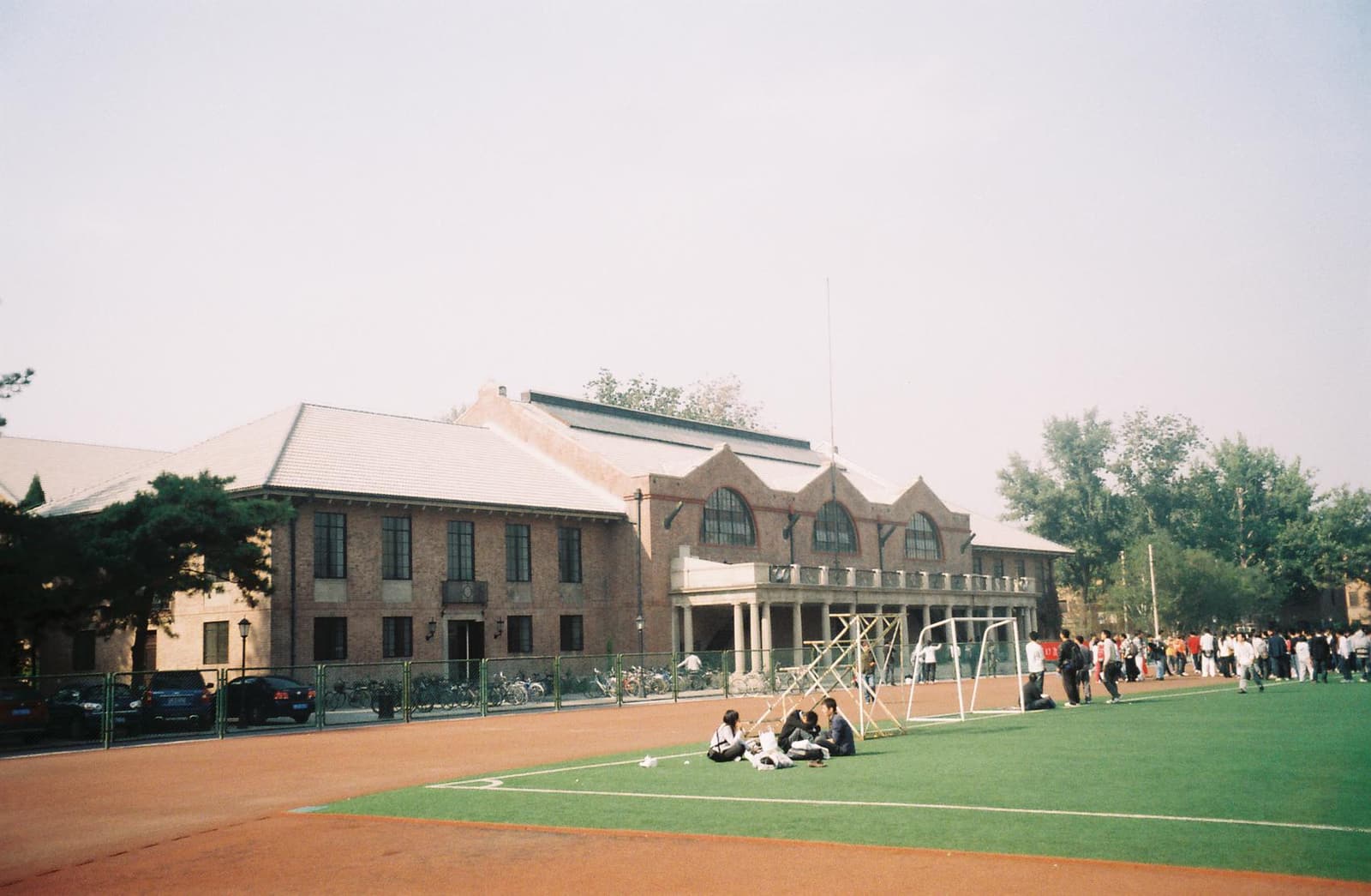 A real photograph of Tsinghua University campus in Beijing, showing athletic fields, trees, and university buildings.