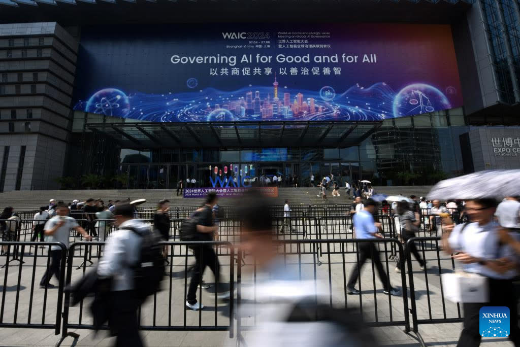 Photograph of people walking outside the WAIC 2024 venue in Shanghai under a large Governing AI for Good and for All banner.