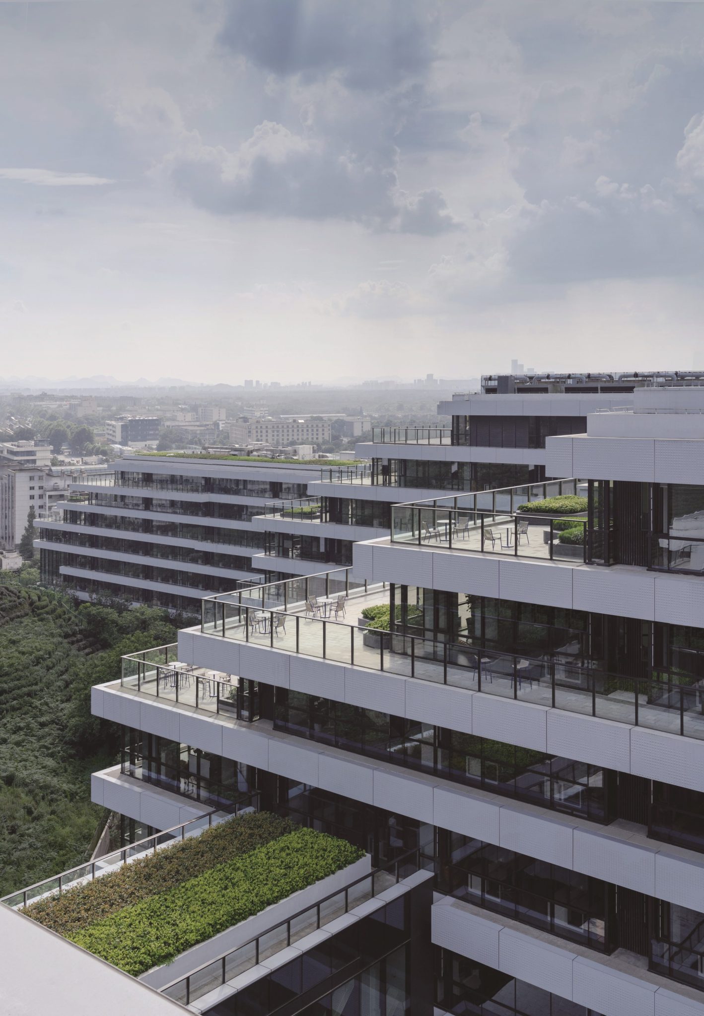 Terraced white buildings at Ant Group's Hangzhou headquarters overlooking green hills and the city.