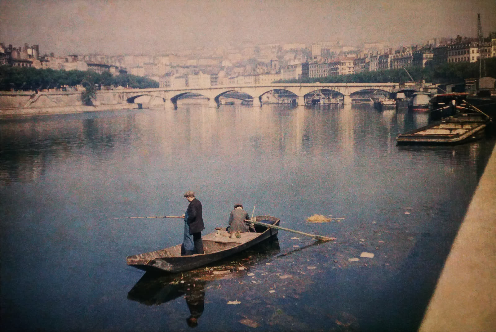 A 1935 Autochrome Lumiere photograph of Lyon's Pont du Change and Quai de Saone, with muted color and a soft grainy surface.