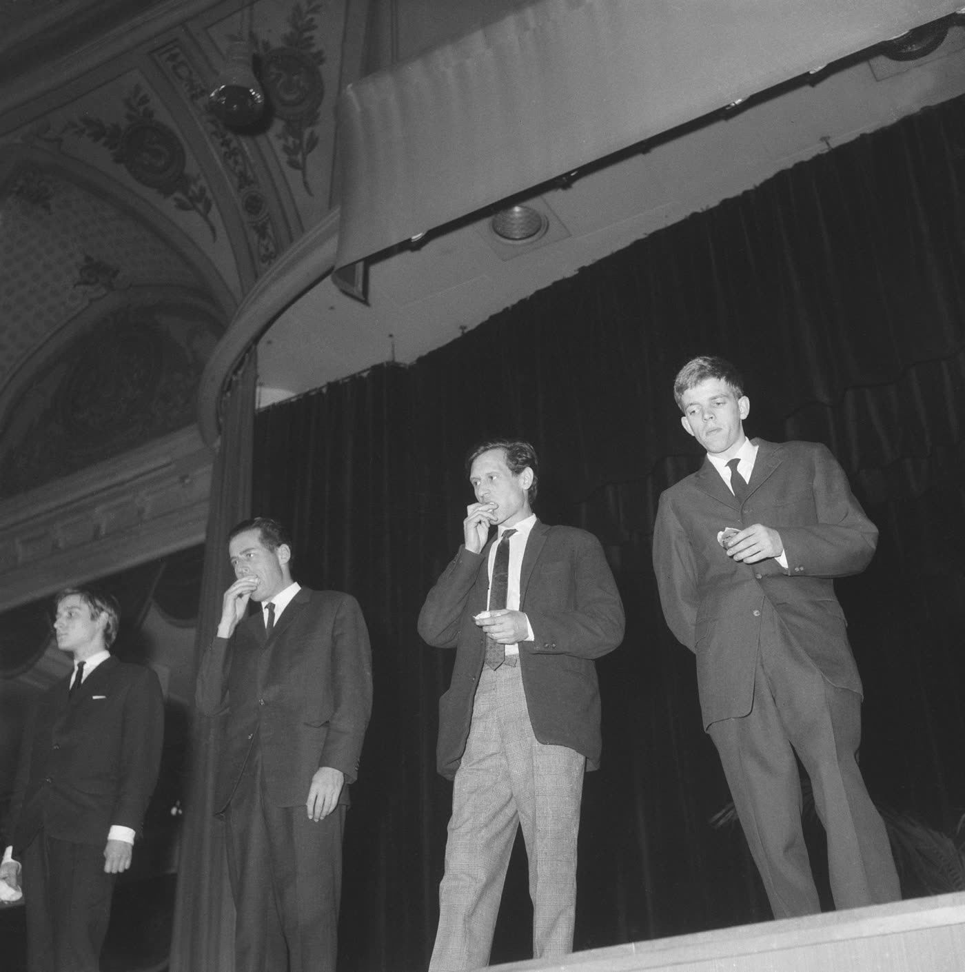 1964 年 Fluxus 表演者在剧场舞台上的黑白档案照片，他们在库尔豪斯斯海弗宁恩的一次音乐会行动中吃潜艇三明治。