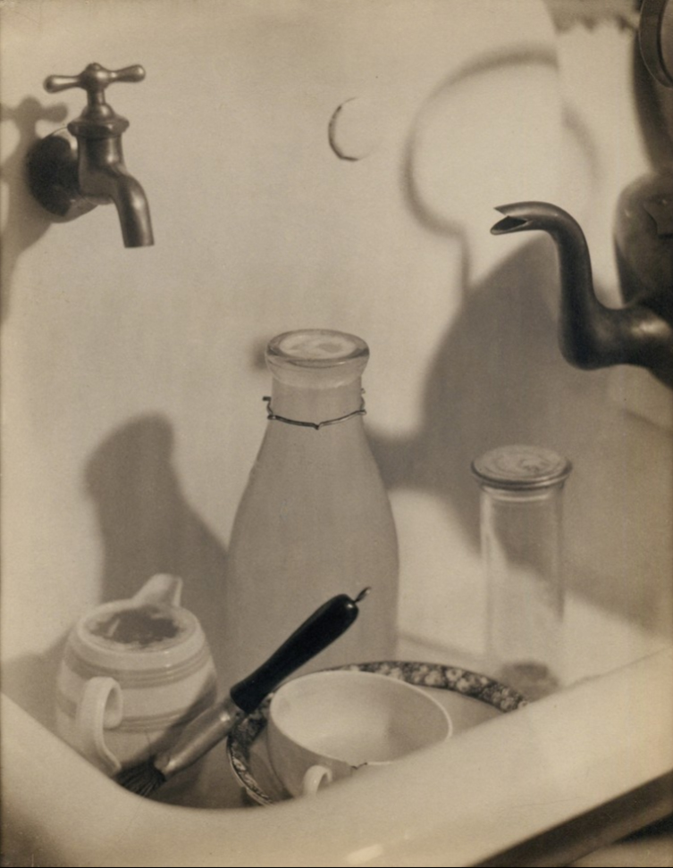 玛格丽特·沃特金斯 1919 年的照片《The Kitchen Sink》，画面中有盘子、瓶子、刷子、水龙头、壶嘴和阴影，它们被安排在浅色水槽盆里。