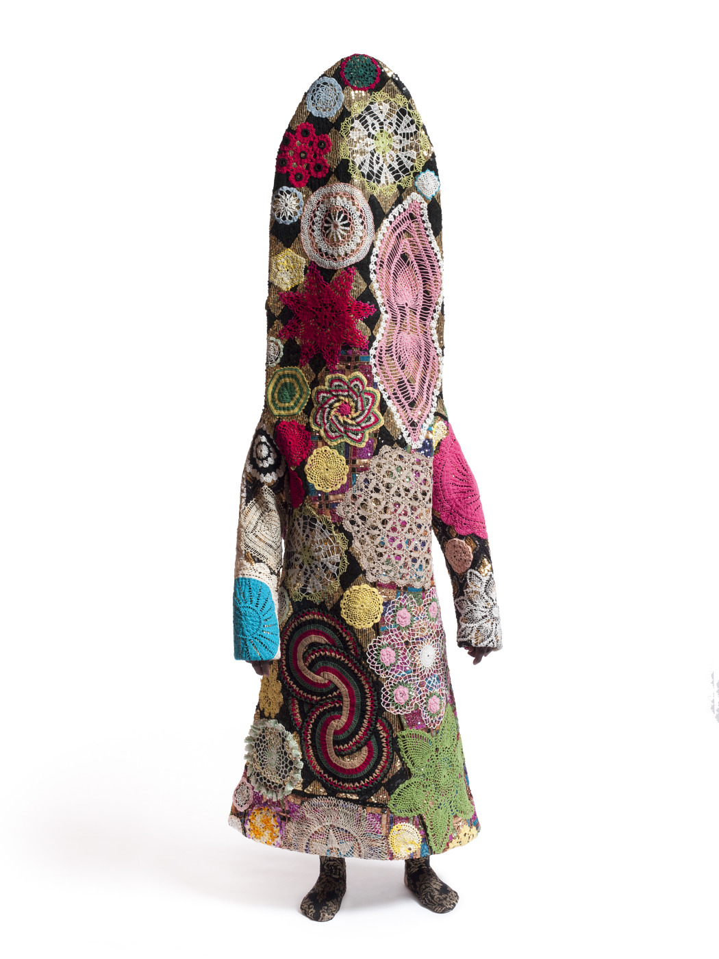 Nick Cave's 2009 Soundsuit, a tall mixed-media wearable sculpture covered in colorful doilies, textile circles, and patterned found material against a plain background.