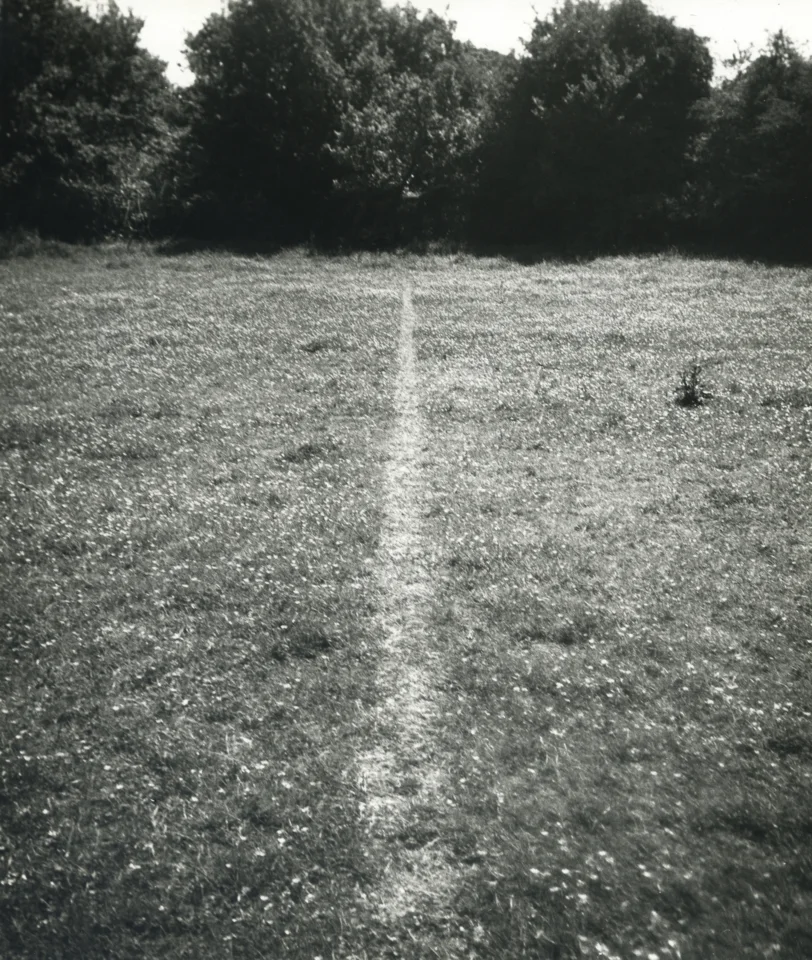 Richard Long's black-and-white photographic artwork A Line Made by Walking, showing a narrow pale line worn through grass toward a low horizon.