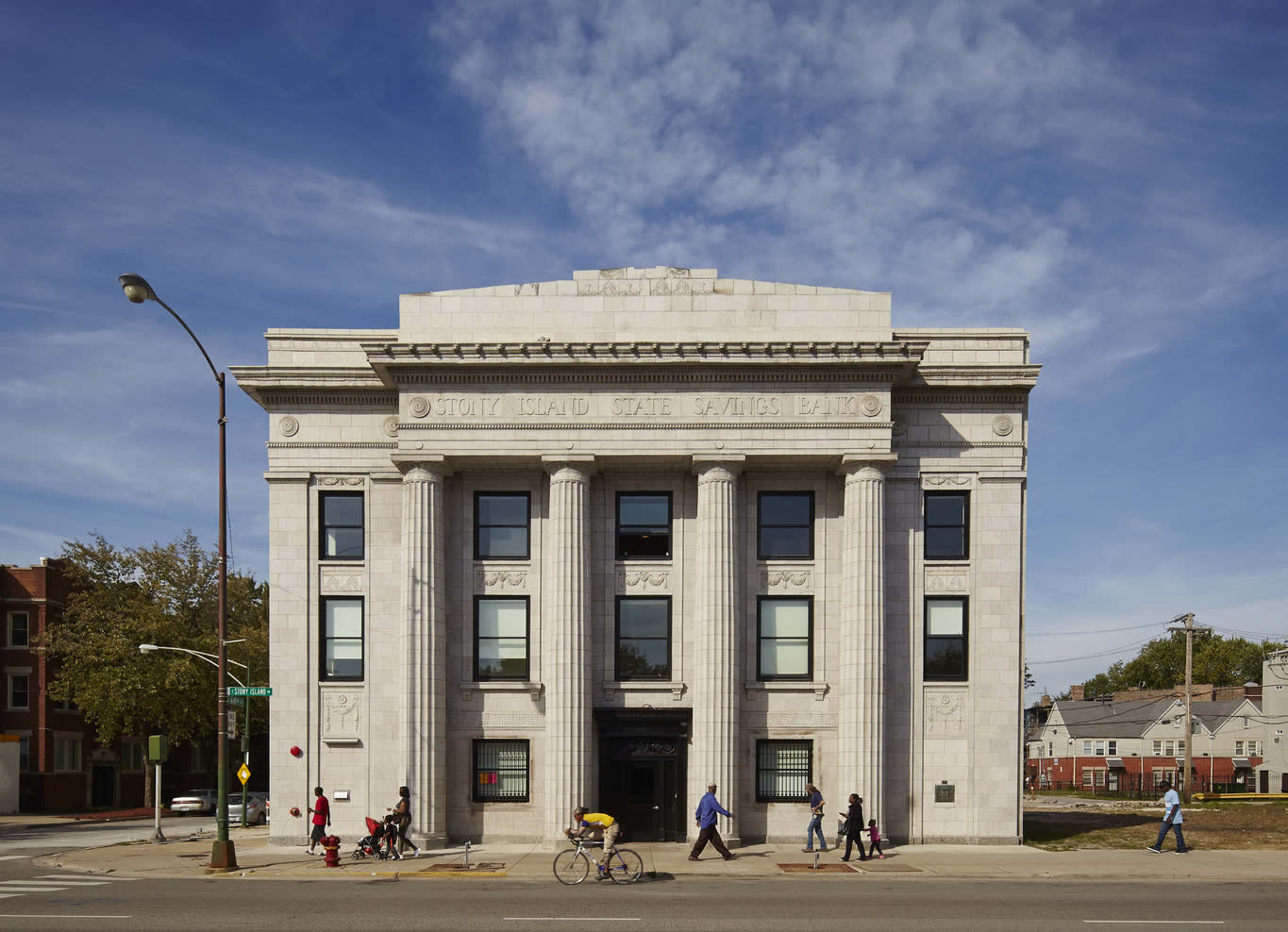 Photograph of the restored Stony Island Arts Bank facade on Chicago's South Side, with pedestrians and a cyclist passing in front.