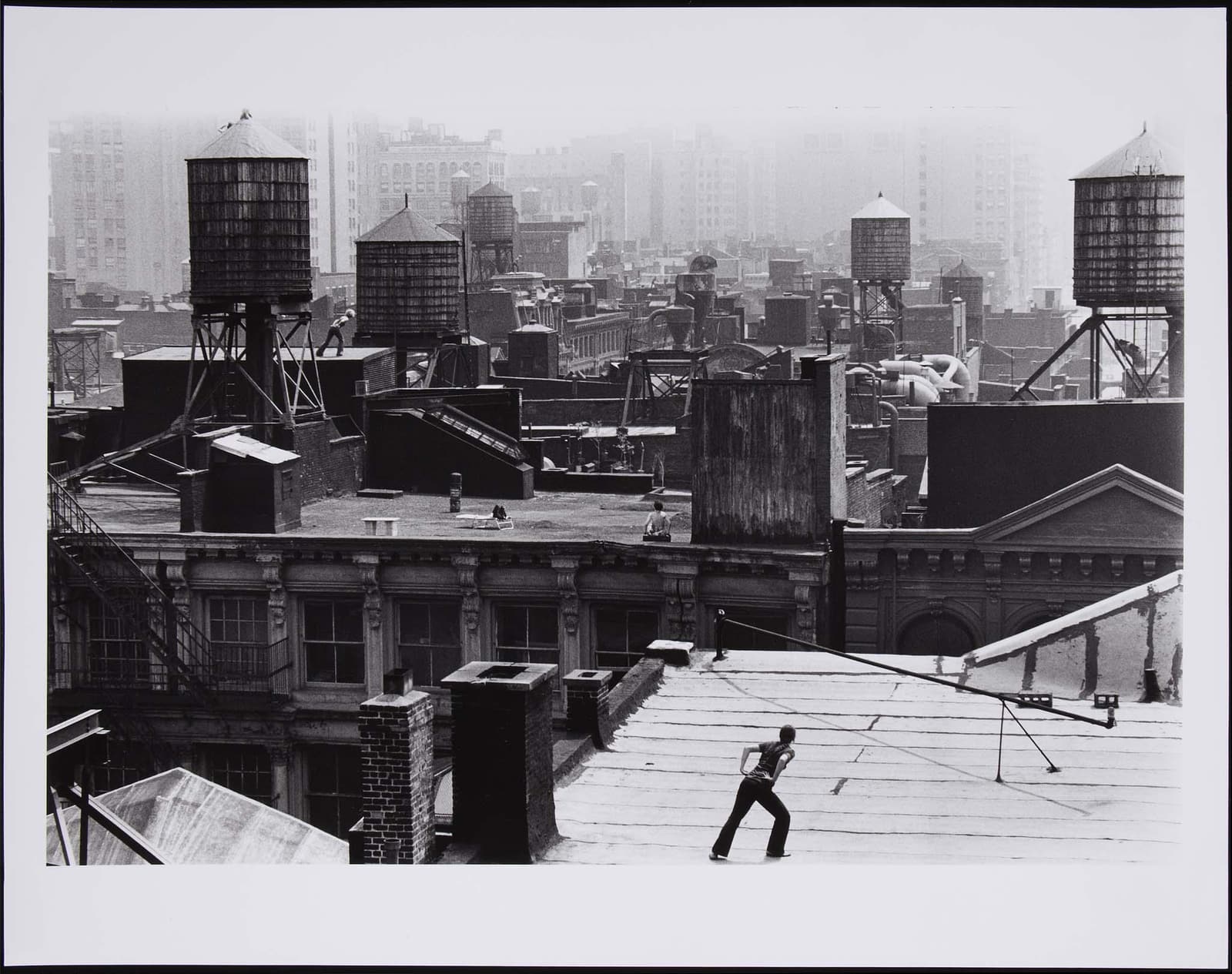 Babette Mangolte's black-and-white photographic documentation of Trisha Brown's Roof Piece, with dancers standing on separate Manhattan rooftops among chimneys and roof structures.