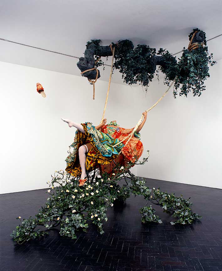 Yinka Shonibare's The Swing (after Fragonard), a headless mannequin in bright Dutch wax printed cotton reclining on a suspended swing with foliage and a flying shoe.