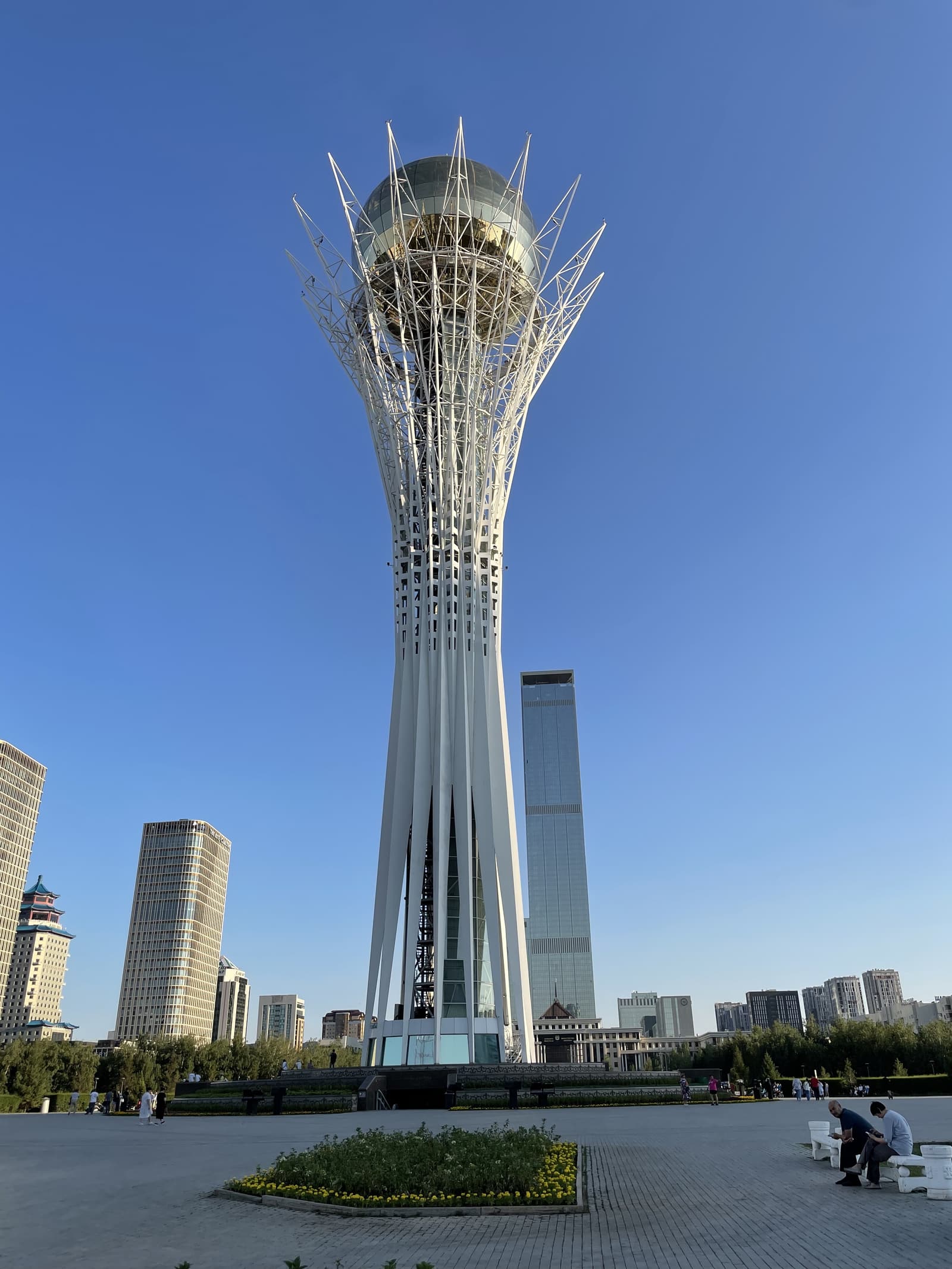 A real photograph of the Baiterek tower in Astana, Kazakhstan, with its golden sphere rising above the plaza.