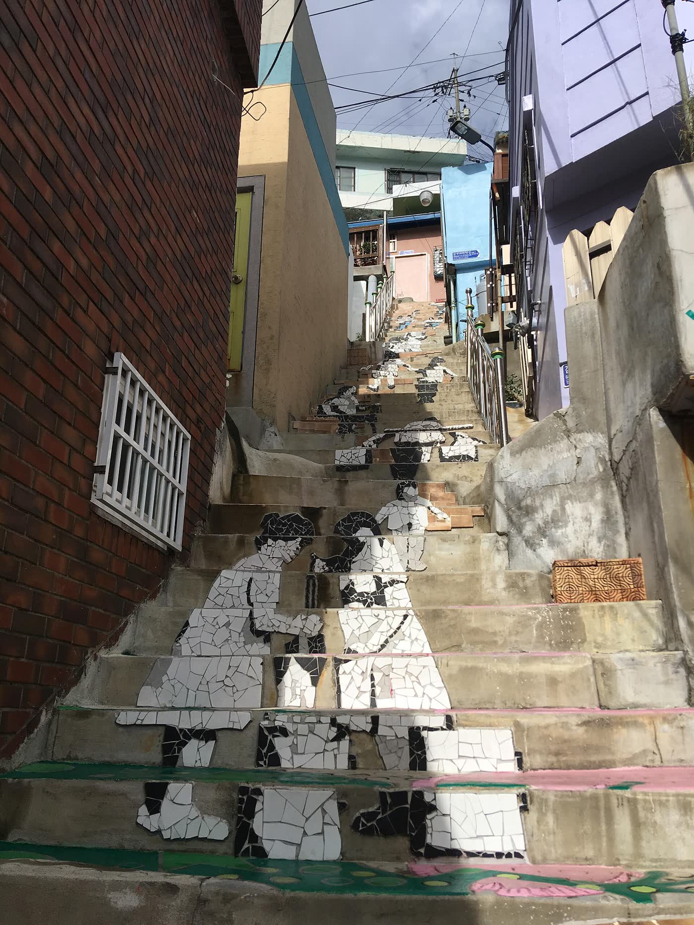 A narrow stair lane rises between painted walls and small houses in Gamcheon Culture Village, Busan.
