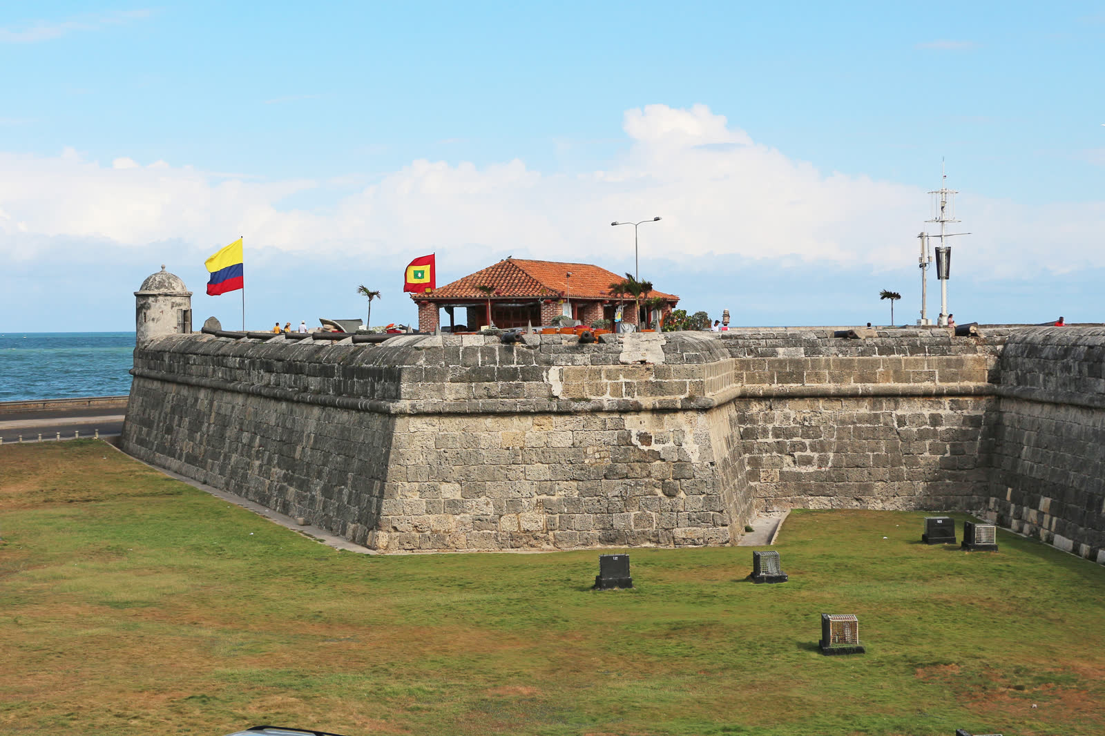 卡塔赫纳的石砌 Santo Domingo 堡垒立在草地护城河上方，背后是加勒比海和哥伦比亚国旗。