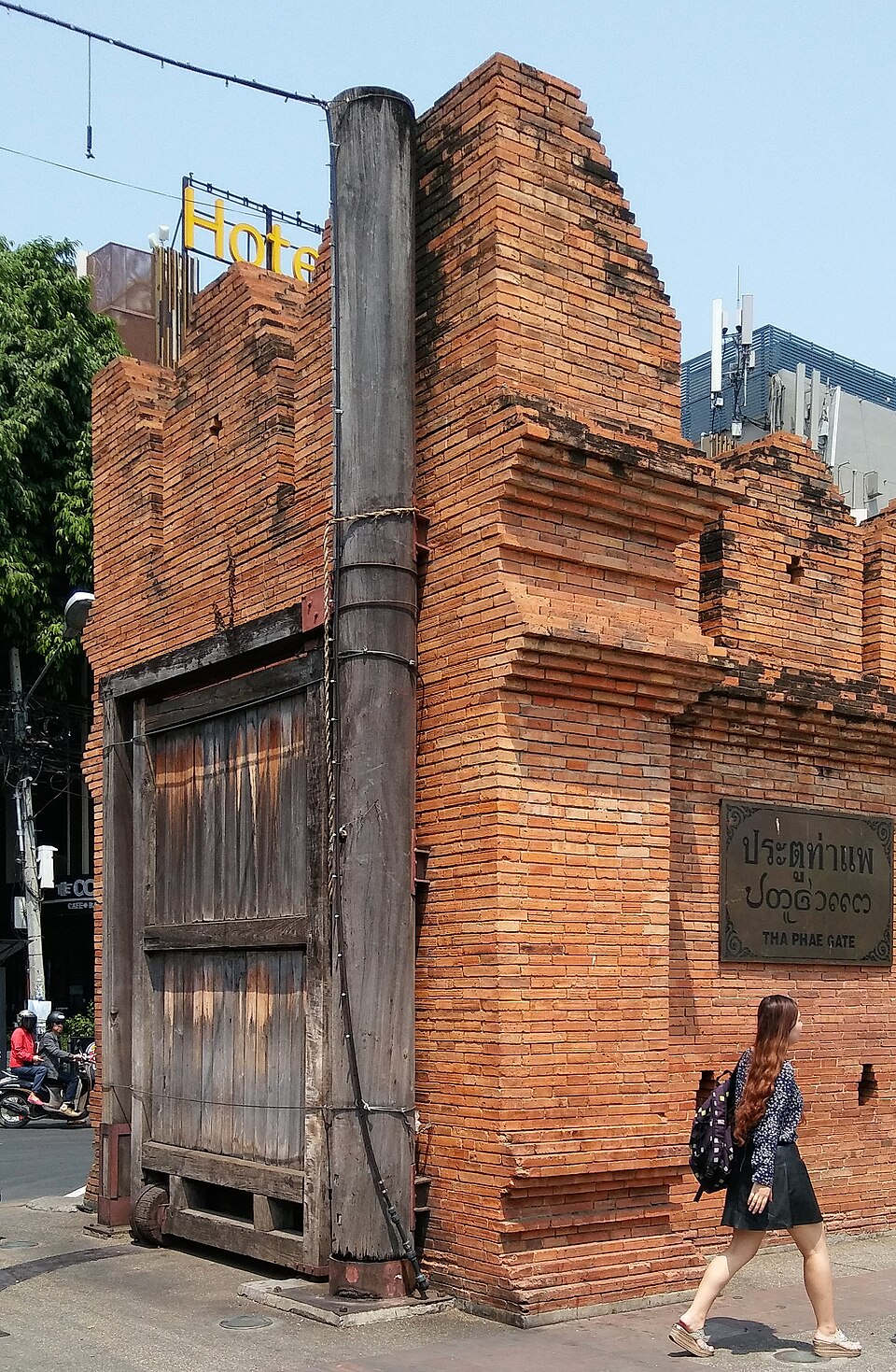 Brick wall and wooden door at Tha Phae Gate in Chiang Mai, with street signage and a pedestrian passing in front.