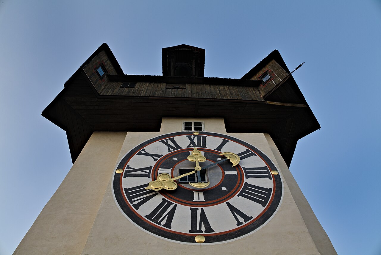 A real evening photograph of the Uhrturm clock tower on the Schlossberg in Graz, with the city visible below.