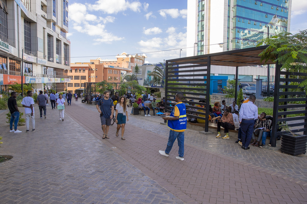 一张真实照片，显示基加利市中心 Imbuga City Walk 沿线的行人、长椅与阴凉座位。