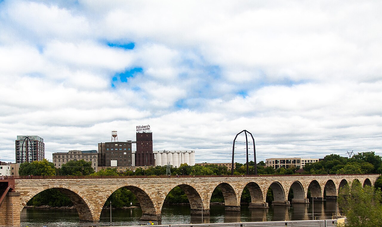 A real photograph of Minneapolis's Stone Arch Bridge spanning the Mississippi River near the historic milling district.