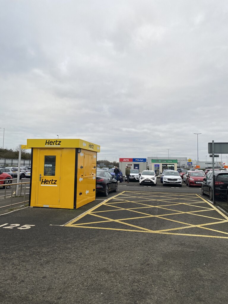 A Hertz rental-car park at Belfast City Airport, with rental cars lined up near branded kiosks.