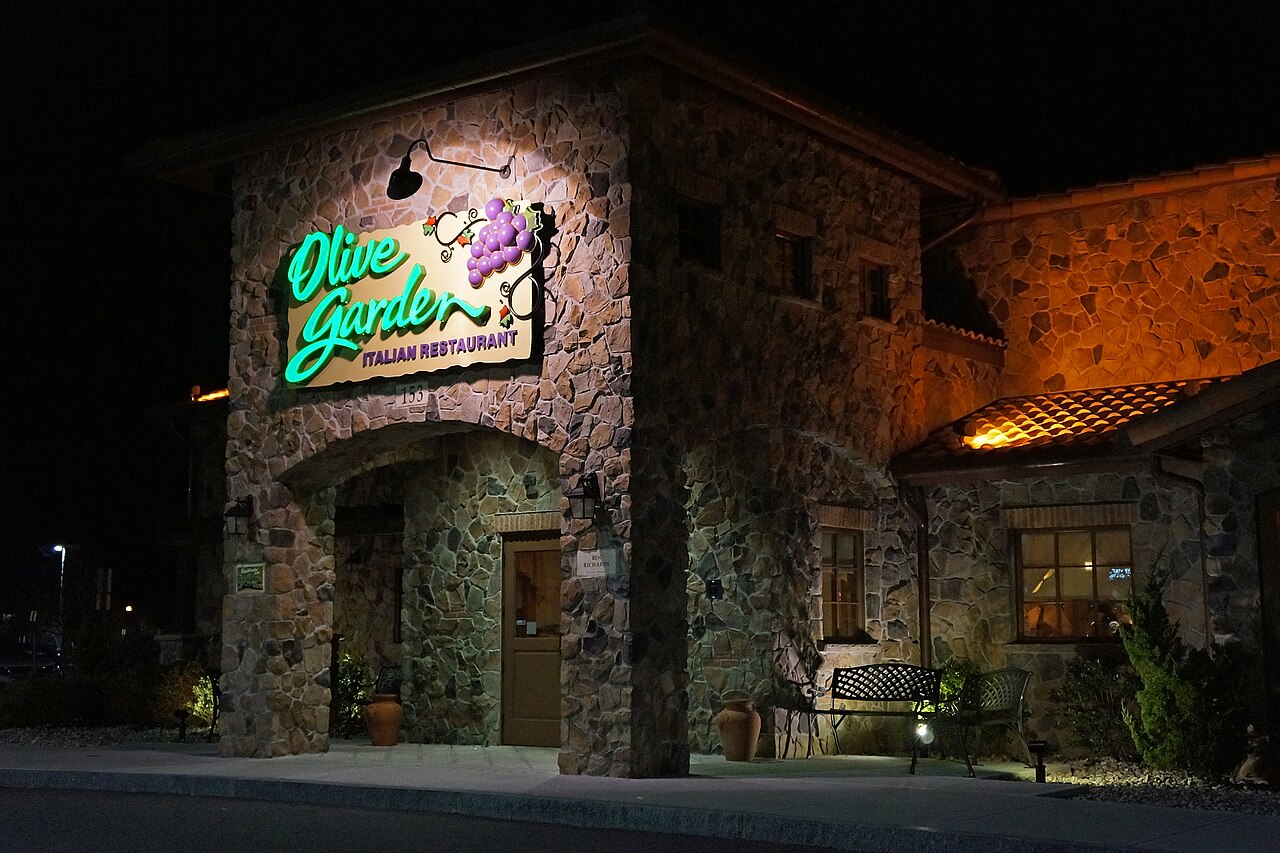 An Olive Garden restaurant exterior photographed at night, with the illuminated green sign above a stone entrance.