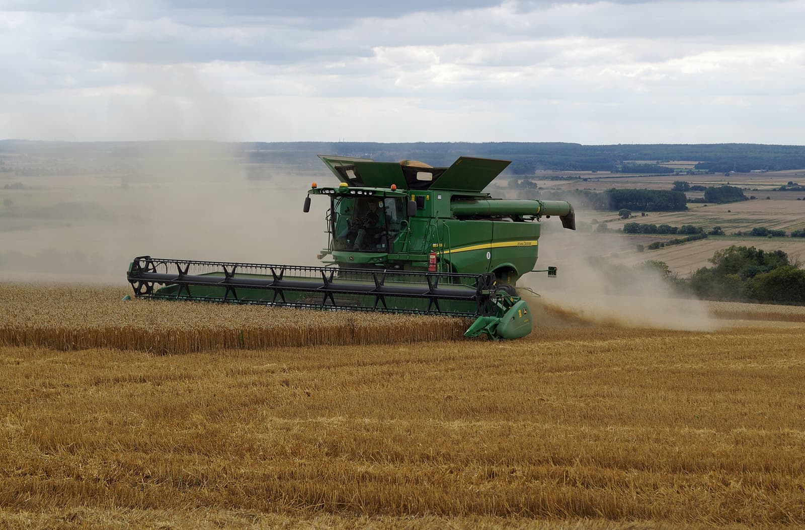 A John Deere combine harvesting a crop field near Worlaby, England, with dust trailing behind the machine.