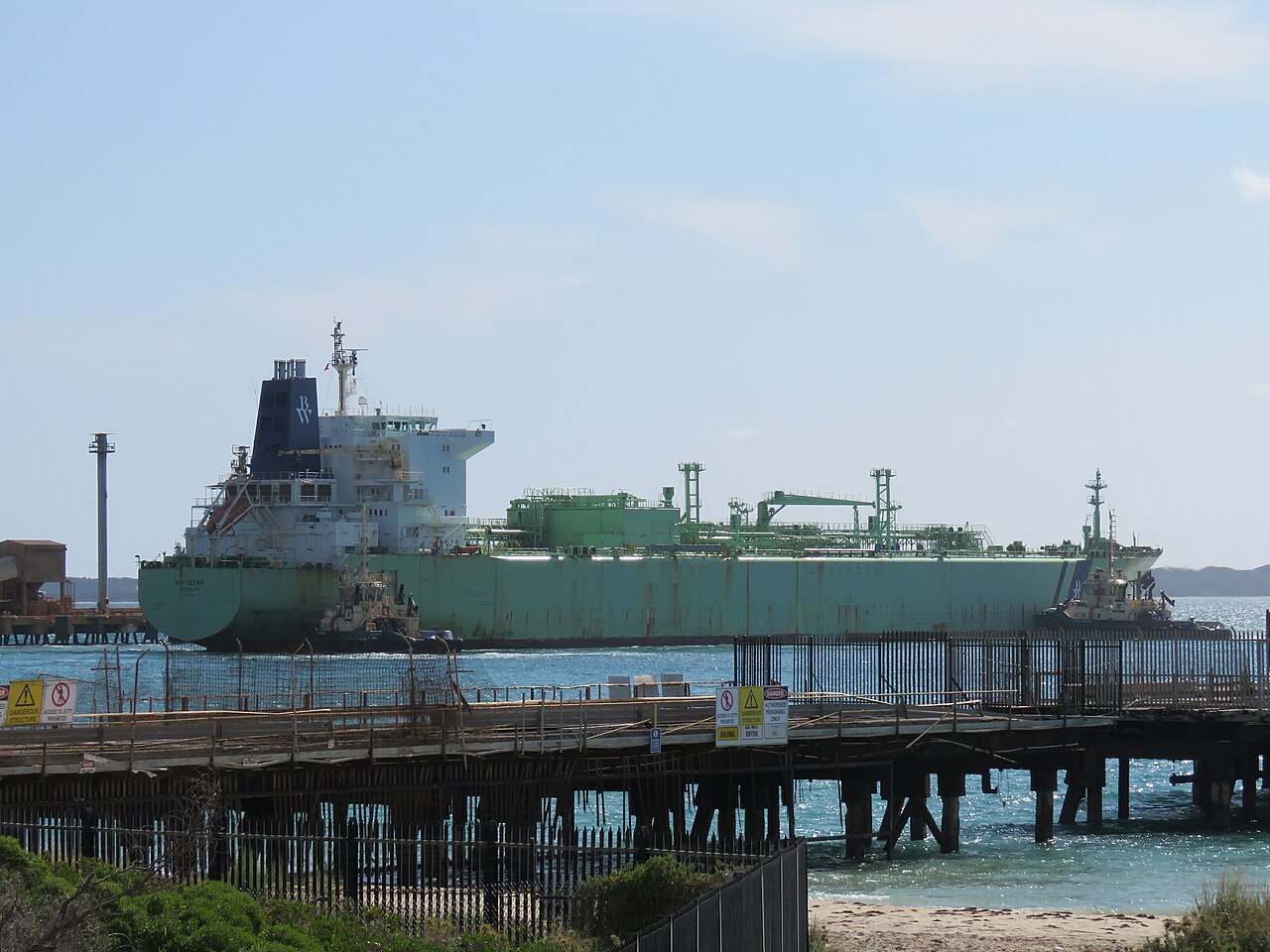 An LPG tanker moored at an industrial bulk terminal with tugs alongside.