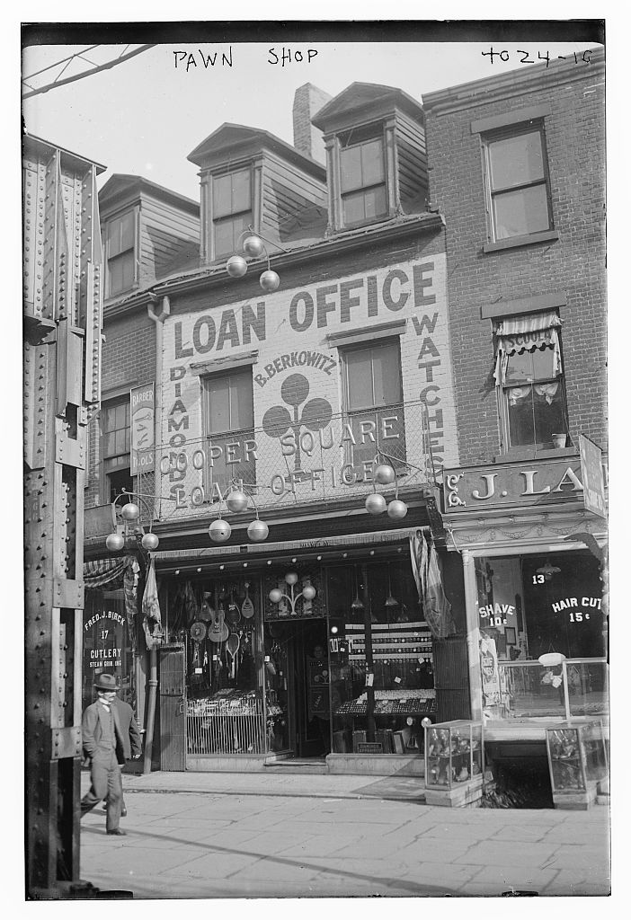Early twentieth-century archival photograph of a pawn shop storefront with watches, jewelry, and signs in the window.